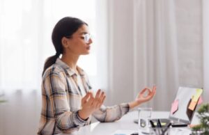 Mulher meditando em frente ao computador para reduzir o estresse no trabalho.