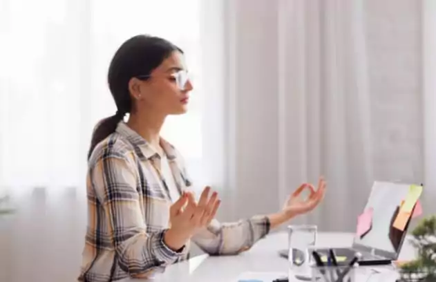 Mulher meditando em frente ao computador para reduzir o estresse no trabalho.
